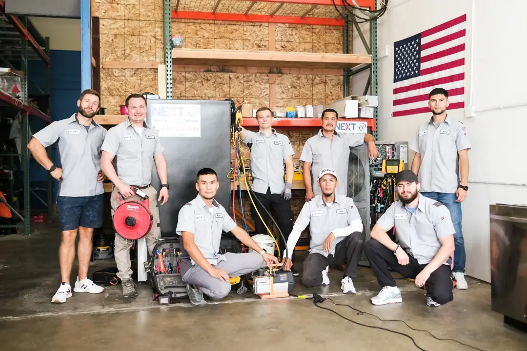 Next HVAC technicians gathered around an air handler and condenser at the company shop
